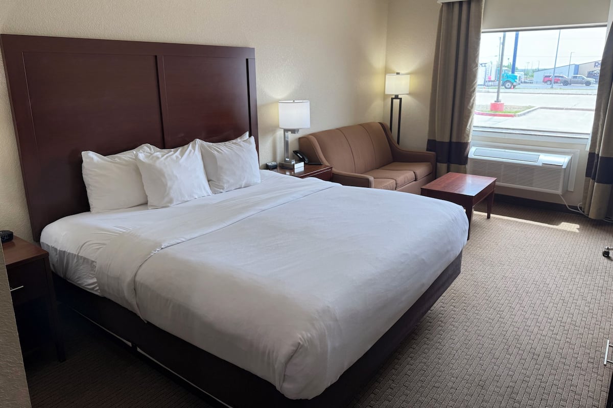 Habitación de hotel con una cama grande, un escritorio, una silla, una lámpara y vistas al exterior.