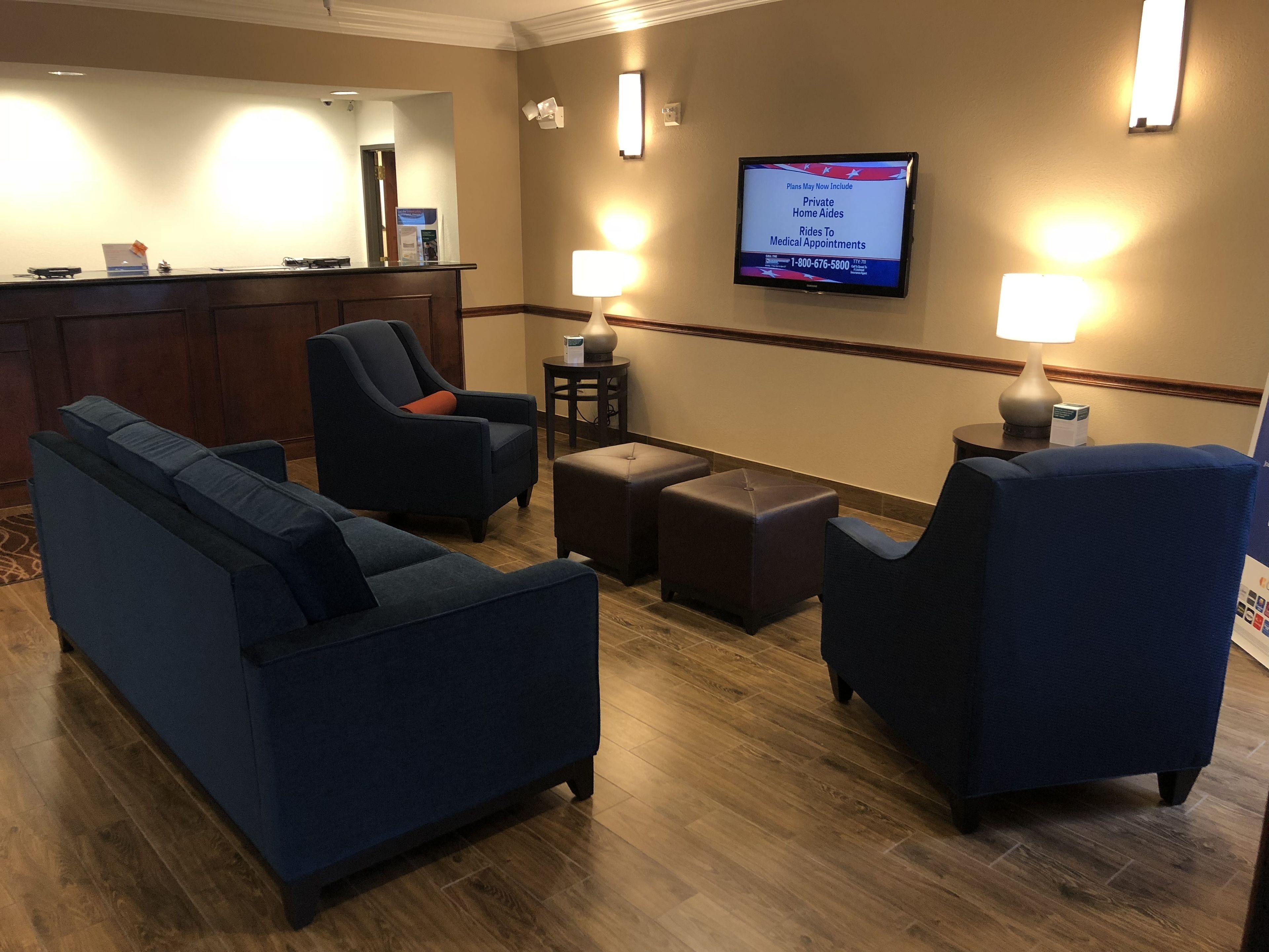 A hotel lobby with a reception desk, seating area with sofas and chairs, and a television displaying information about services.