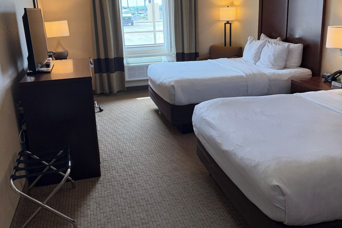 Habitación de hotel con dos camas, un escritorio, una silla y vista a la calle.