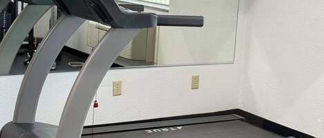 A treadmill in a gym with a mirror reflecting the room.