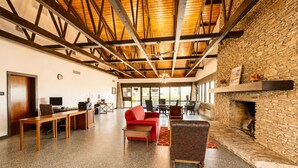 A spacious room with a high ceiling, stone wall, fireplace, and a seating area with a red sofa and chairs. - Segovia Lodge Junction TX I -10 (Junction)