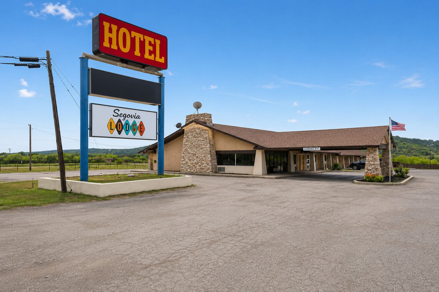 Un hotel llamado Segovia Lodge con fachada de piedra, cielo despejado y una bandera estadounidense.