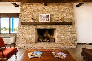A stone fireplace with a framed photo above, a wooden bench, and a table with magazines. - Segovia Lodge Junction TX I -10 (Junction)
