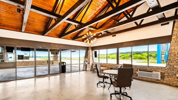 A spacious room with a high ceiling, large windows, and a stone wall. - Segovia Lodge Junction TX I -10 (Junction)