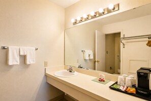 A hotel bathroom with a sink, mirror, towel rack, and a coffee machine. - Segovia Lodge Junction TX I -10 (Junction)