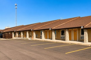 A motel with multiple rooms, a parking lot, and a cell tower in the background. - Segovia Lodge Junction TX I -10 (Junction)