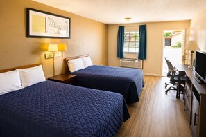 Quarto de hotel com duas camas, uma escrivaninha com computador, televisão, janela com cortinas e ar condicionado.