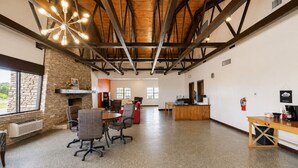 A spacious room with a stone fireplace, wooden ceiling beams, and a large window. - Segovia Lodge Junction TX I -10 (Junction)