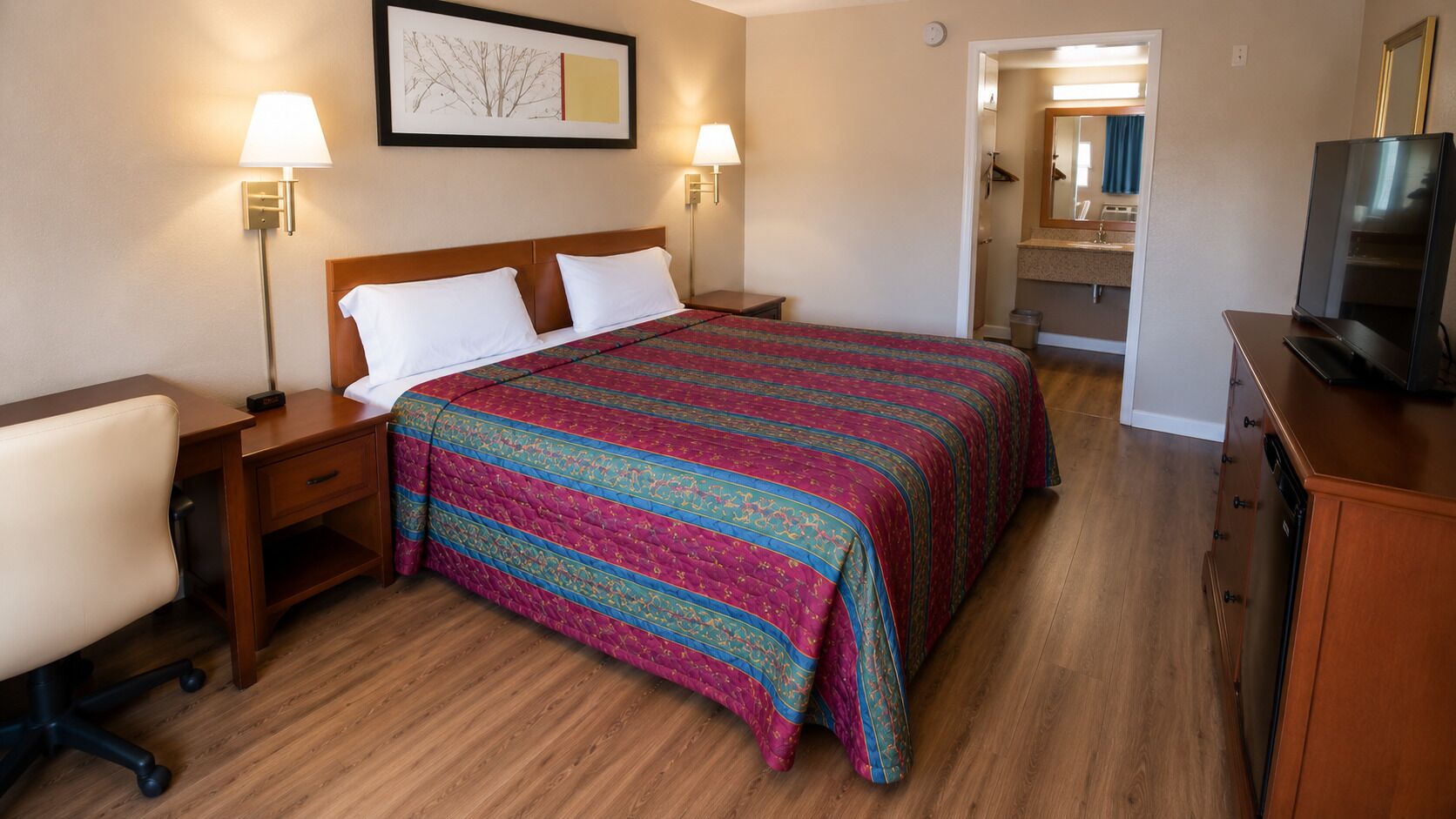 Een hotelkamer met een bed, nachtkastjes, een bureau, een stoel, een televisie en een badkamer die door een geopende deur zichtbaar is.