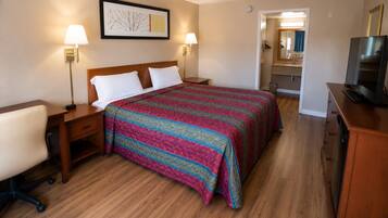 Een hotelkamer met een bed, nachtkastjes, een bureau, een stoel, een televisie en een badkamer die door een geopende deur zichtbaar is.