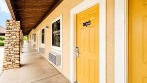 A hotel corridor with stone pillars, yellow doors, and a covered walkway. - Segovia Lodge Junction TX I -10 (Junction)