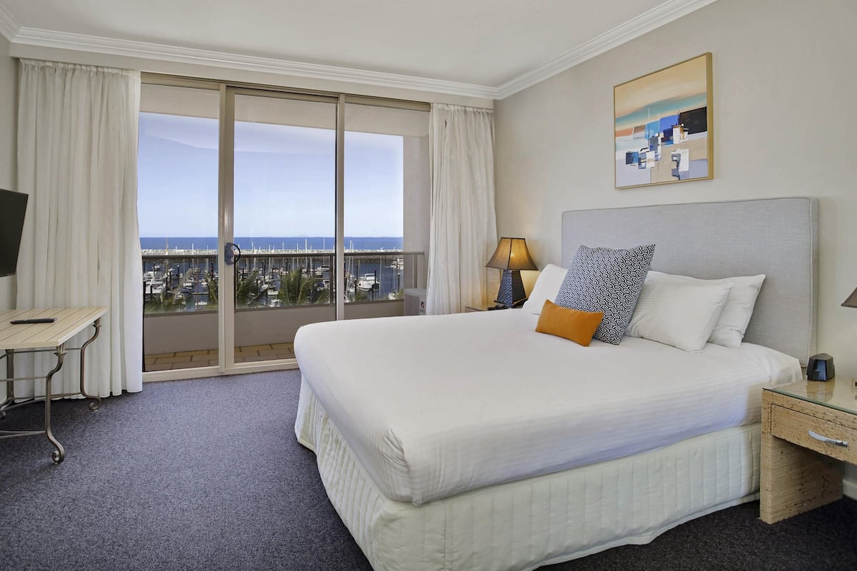 A hotel room with a bed, a desk, a lamp, a nightstand, and a painting.