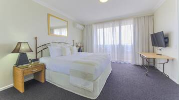 Ein Hotelzimmer mit einem Bett, einem Nachttisch mit Lampe, einem Fernseher auf einem Standfuß und einem Fenster mit Vorhängen.