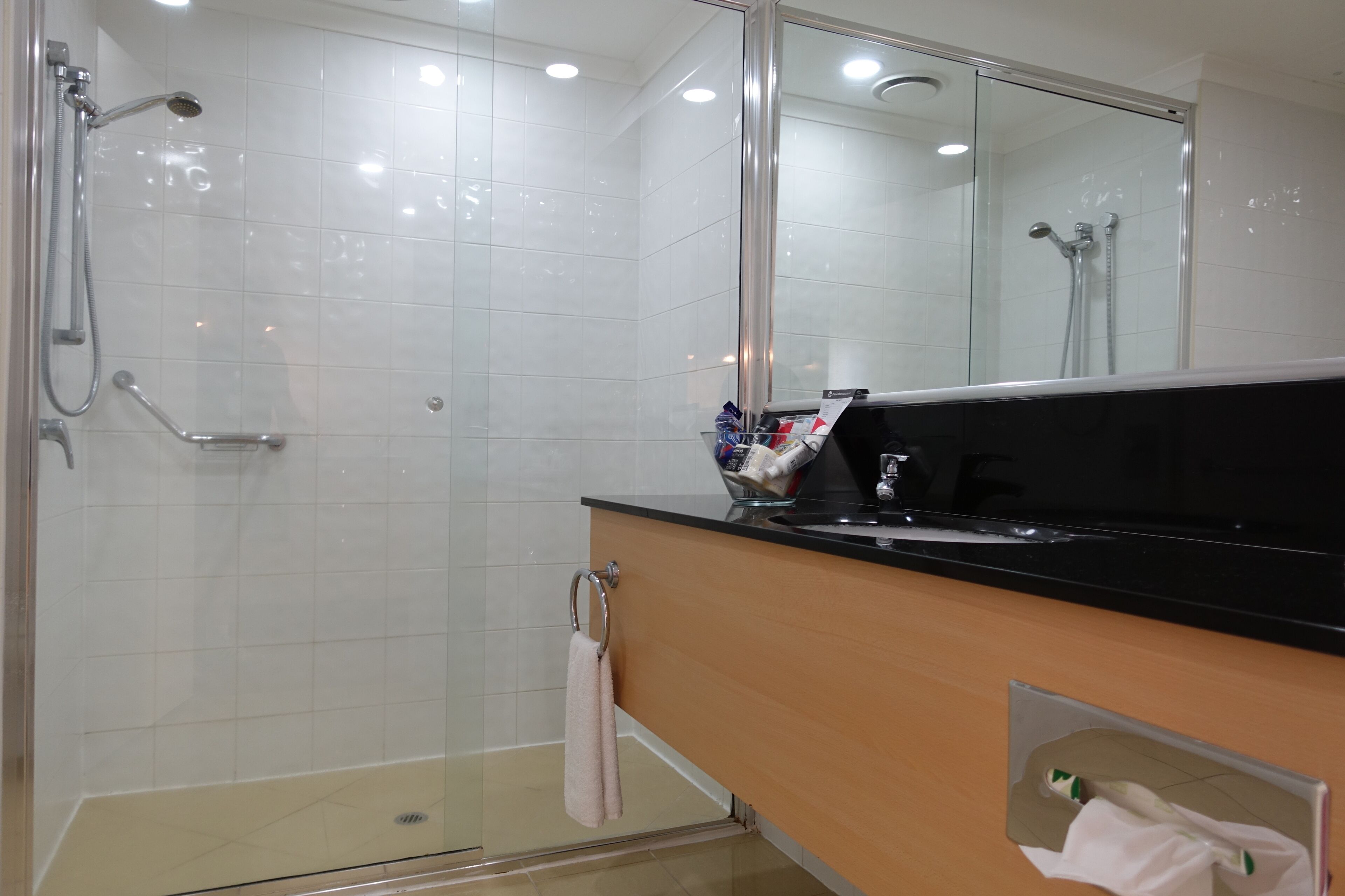 A modern bathroom with a glass shower enclosure, a black countertop, and a large mirror.
