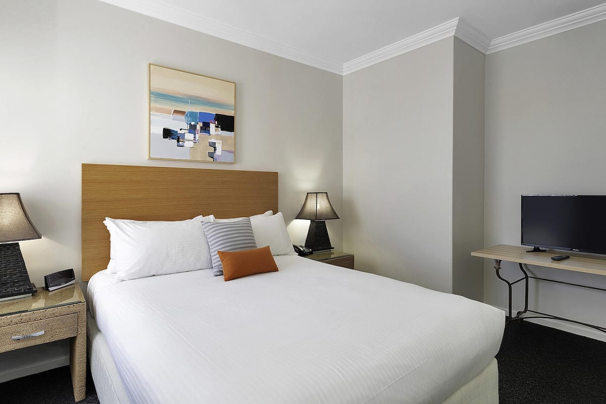 A hotel room with a bed, two bedside tables, a television, and a painting on the wall.