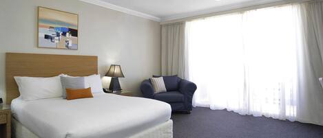 A hotel room with a bed, a nightstand, a lamp, a chair, and a large window with curtains.