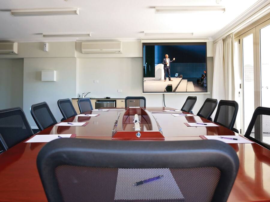 A conference room with a long table, chairs, a projector screen, and a window with curtains.
