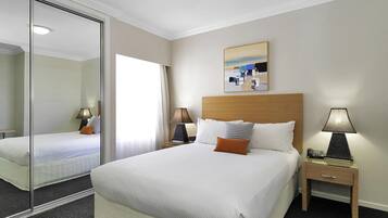 A hotel room with a large bed, a bedside table with a lamp, a bedside phone, a mirror, and a painting on the wall.