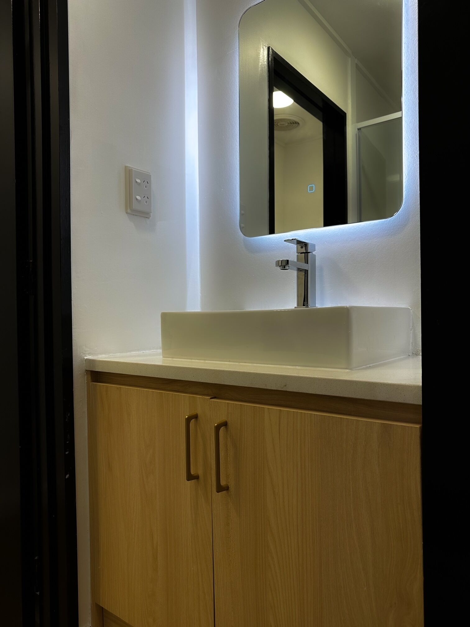 Un baño con un lavamanos blanco, un espejo y armarios de madera.