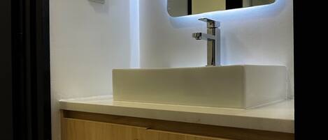 Un baño con un lavamanos blanco, un espejo y armarios de madera.