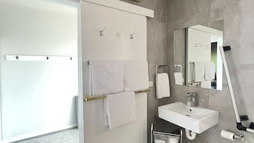 A modern bathroom with a white sink, a mirror, a towel rack, and a shower area.