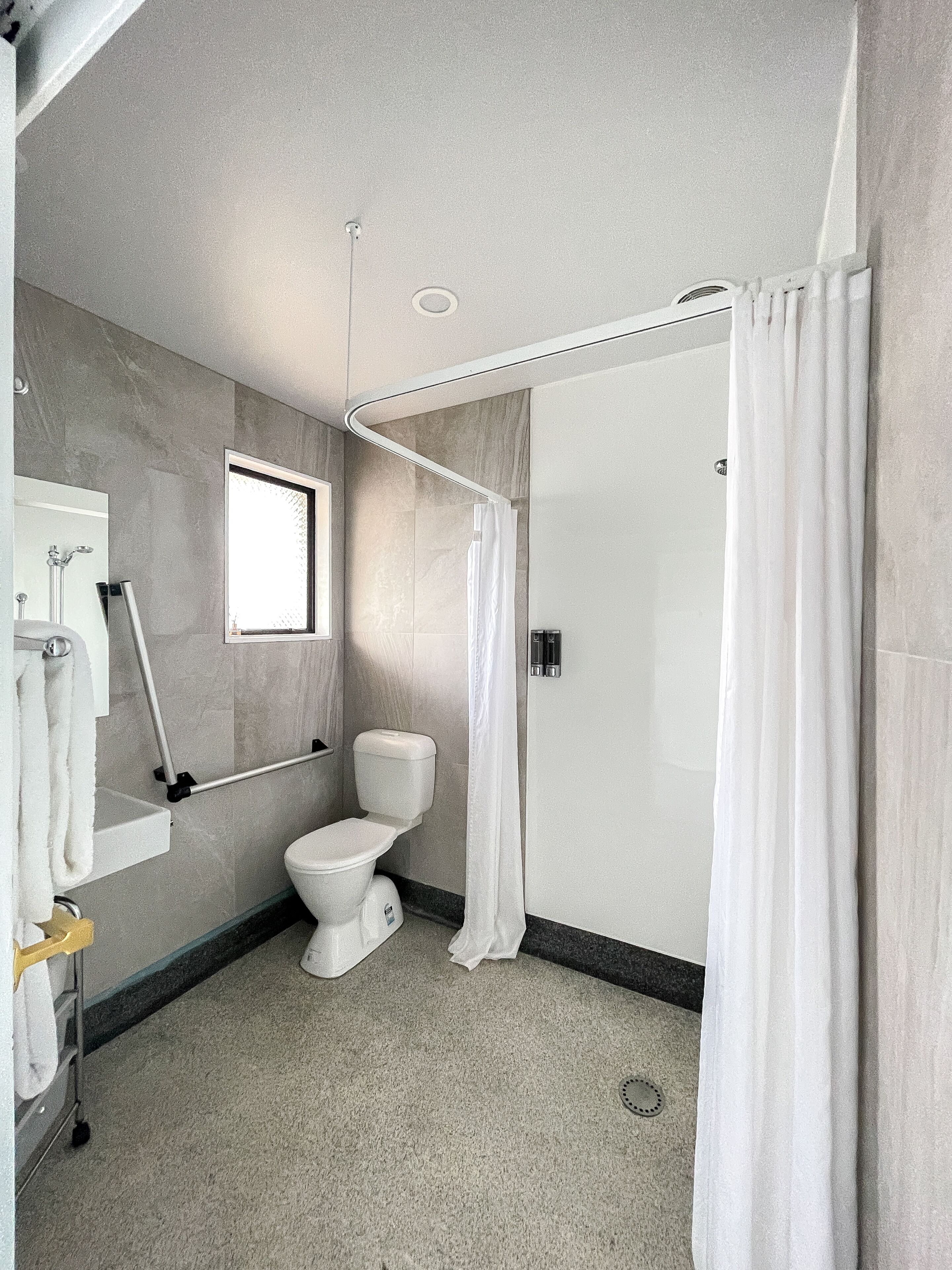 Ein modernes Badezimmer mit Toilette, einer Duschkabine, einem Handtuchhalter und einem Spiegel.