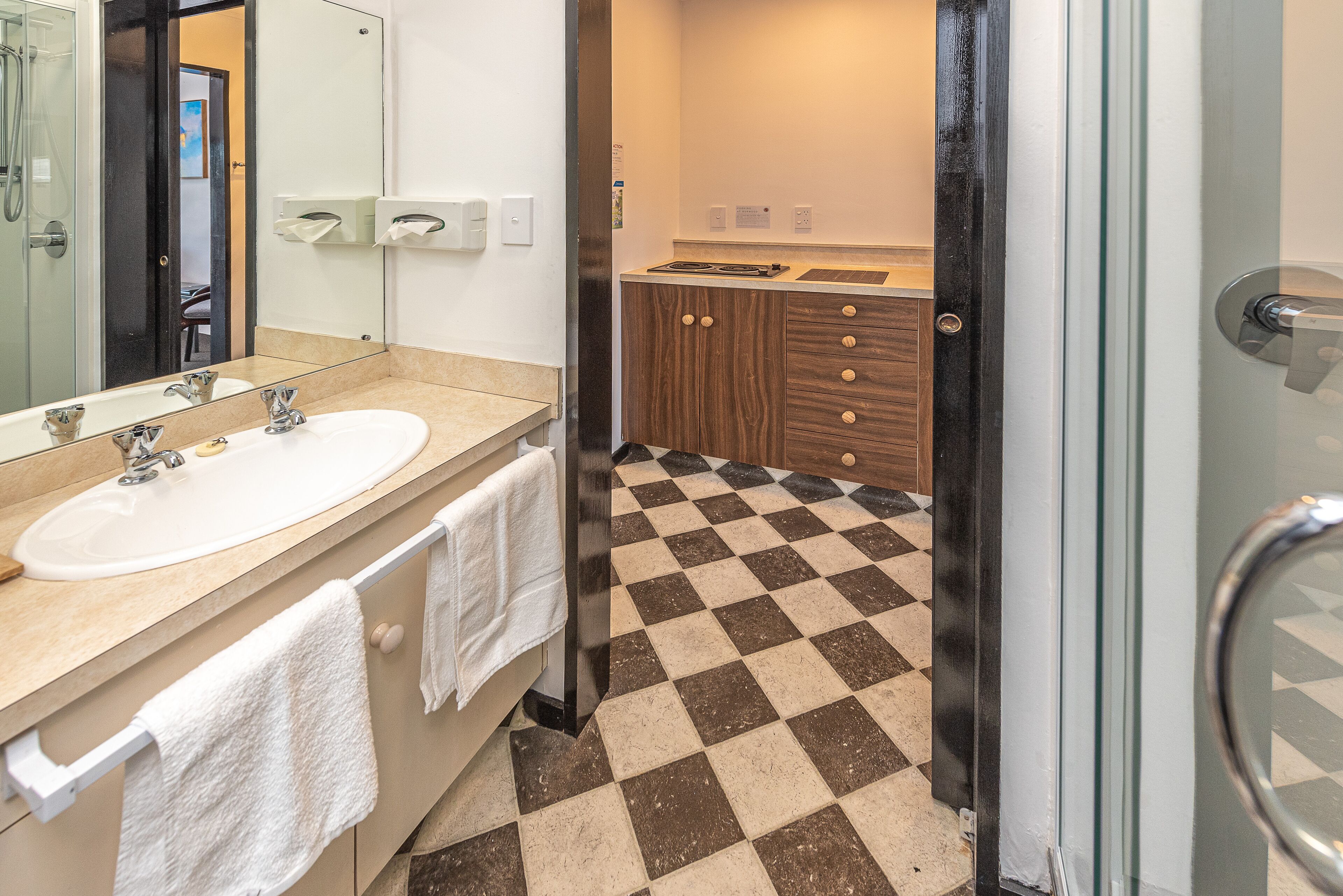 Un baño con un espejo grande, un lavamanos y un piso a cuadros.