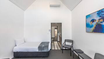A hotel room with a bed, a chair, a desk, and a painting on the wall.