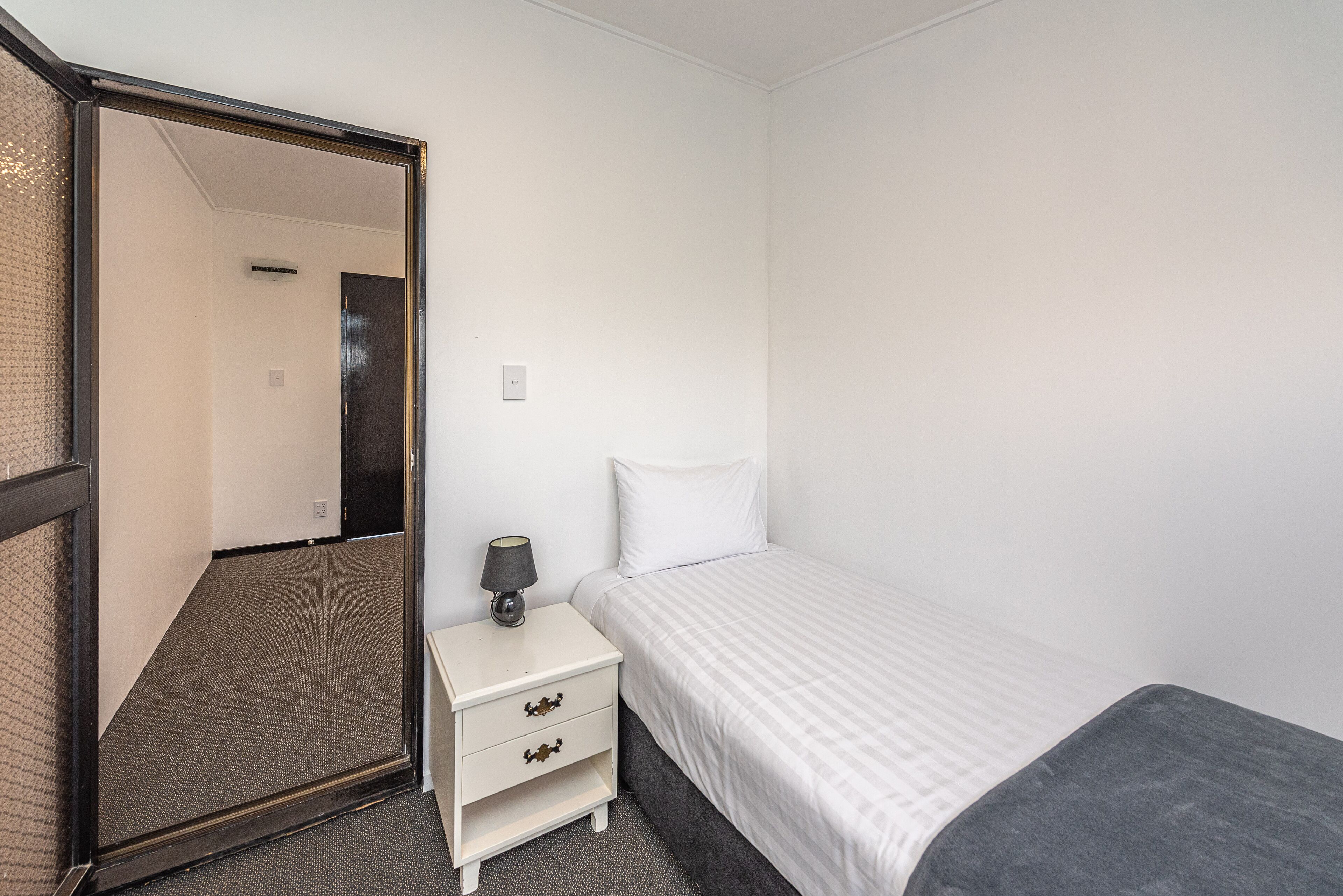 A bedroom with a bed, a nightstand with a lamp, and a mirror.