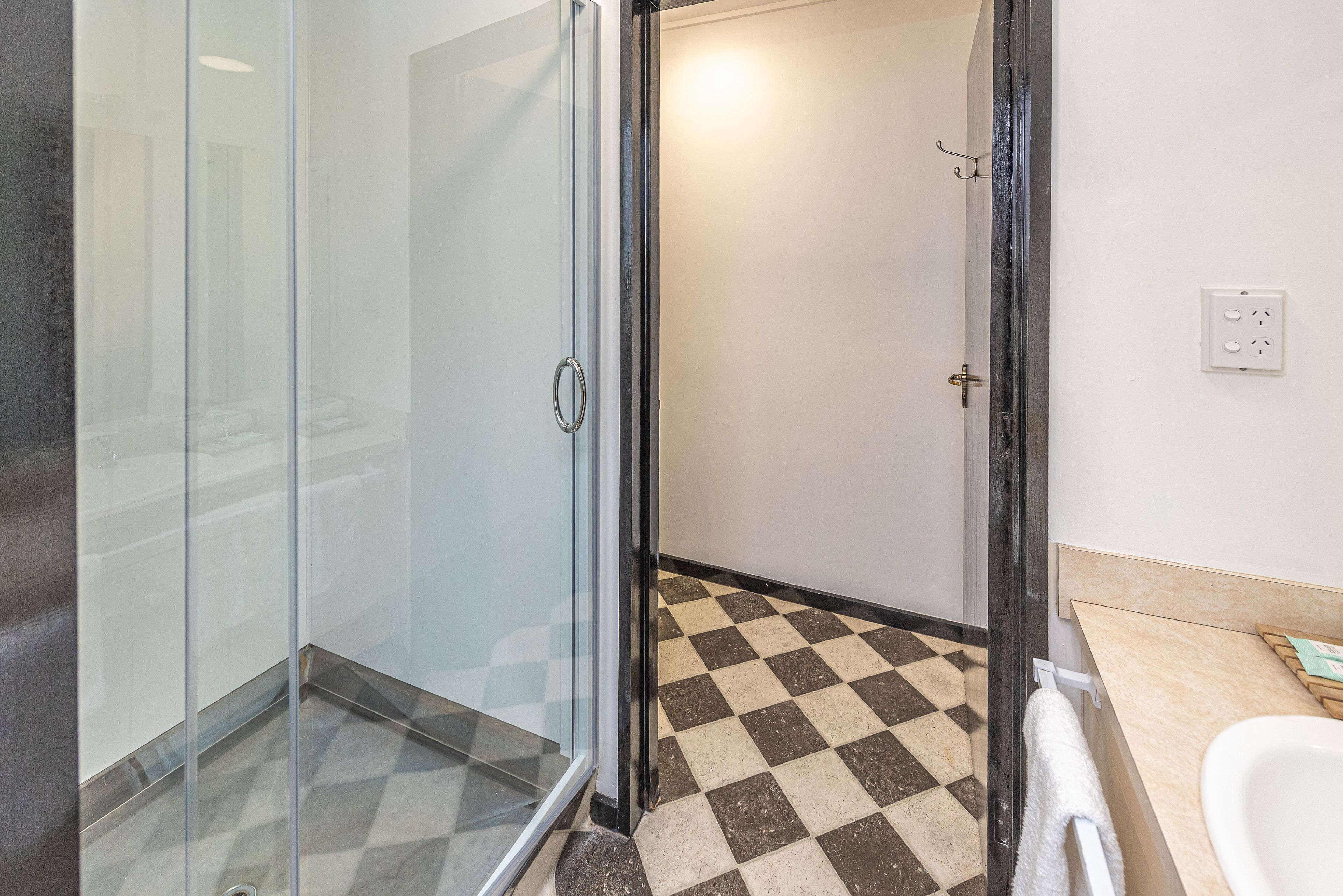 Un baño con cabina de ducha de vidrio, suelo a cuadros y lavamanos blanco.