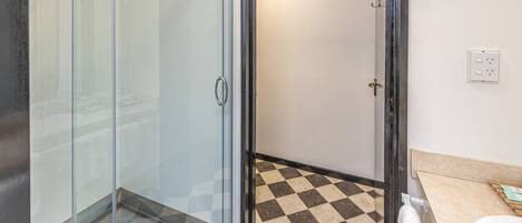 Un baño con cabina de ducha de vidrio, suelo a cuadros y lavamanos blanco.
