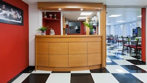 Un espace d’accueil doté d’un comptoir en bois, d’un sol à carreaux et d’un coin salon avec des tables et des chaises.
