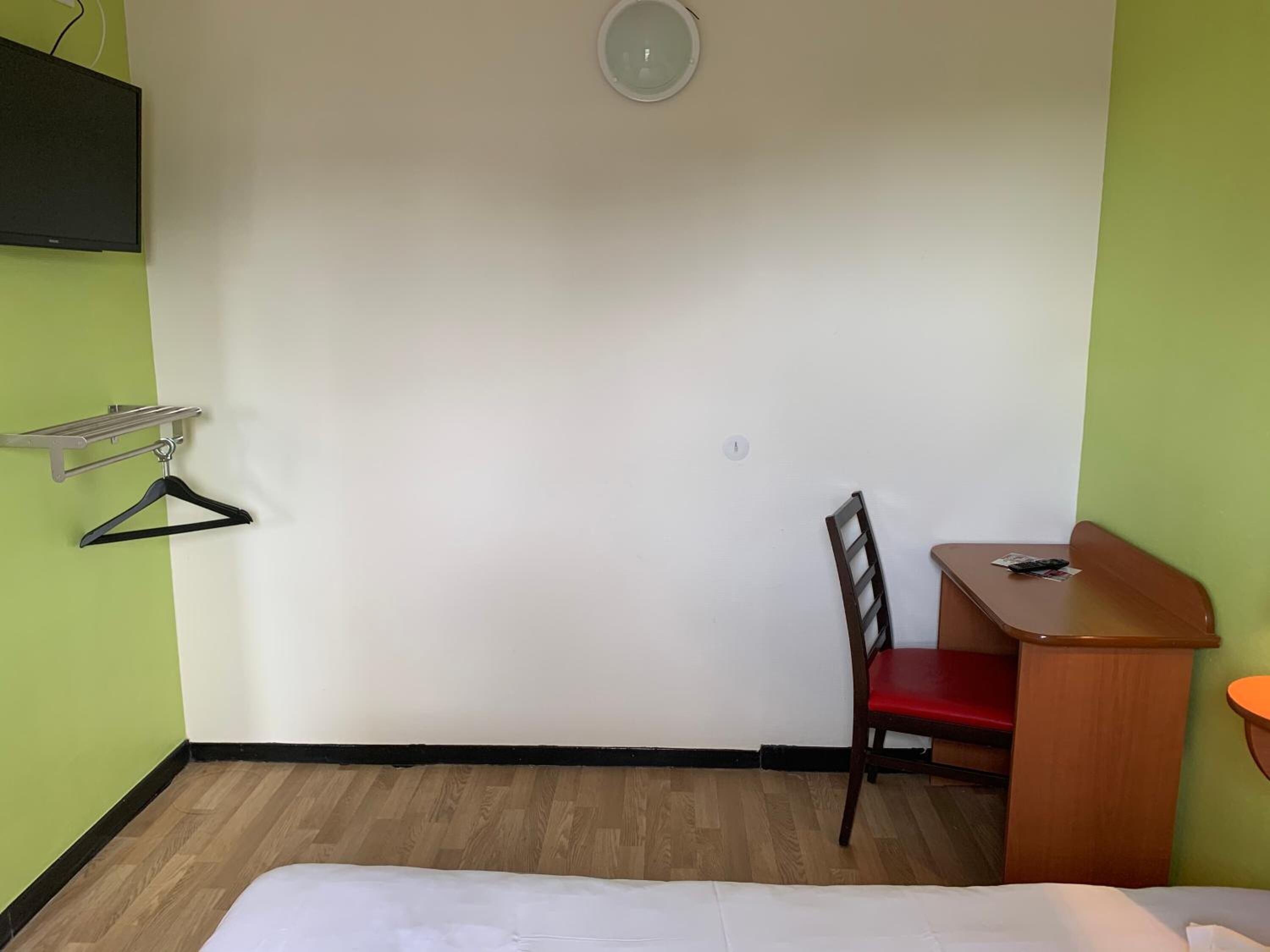 A small, simple room with a bed, a desk, a chair, and a TV mounted on the wall.