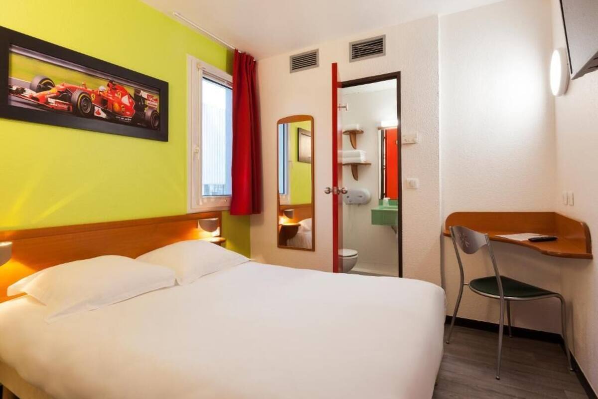 Une chambre d’hôtel comprenant un lit, un bureau, une chaise, une salle de bain et un miroir.