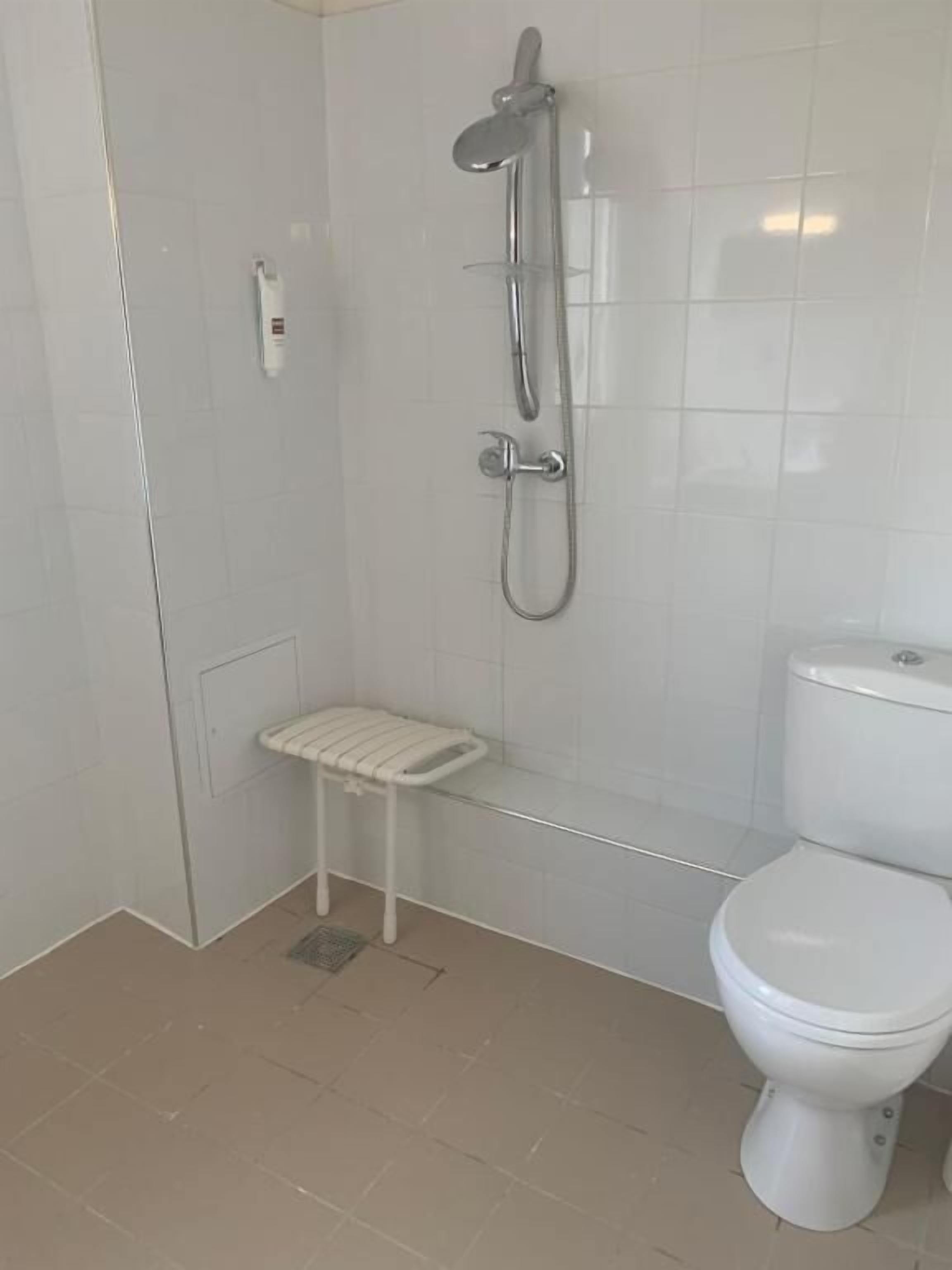 A bathroom with a toilet, a shower, and a small stool.