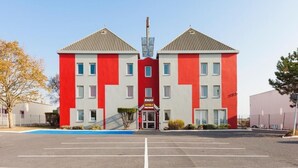 Un hôtel aux couleurs rouge et blanche, avec une entrée centrale et un parking situé devant.