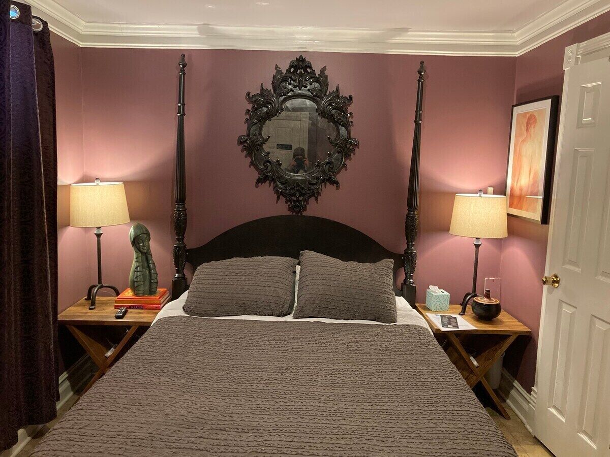 Un dormitorio con cama con dosel, dos mesitas de noche, un espejo y una puerta.