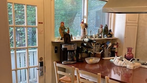 Una cocina con una mesa de madera, cuatro sillas de madera, una cafetera y diversos utensilios de cocina.