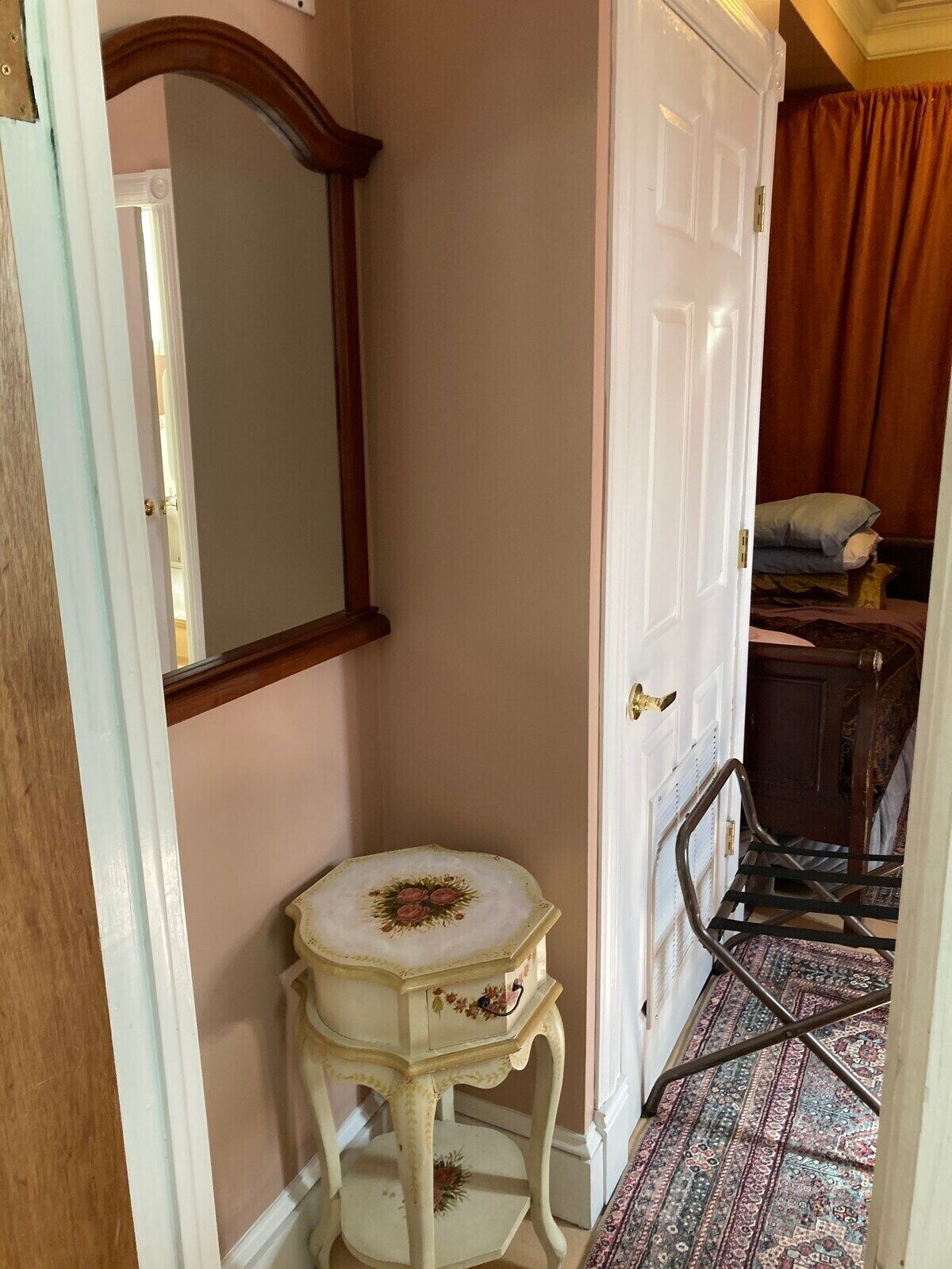 A narrow hallway with a white door, a small round table with floral decoration, and a patterned carpet.