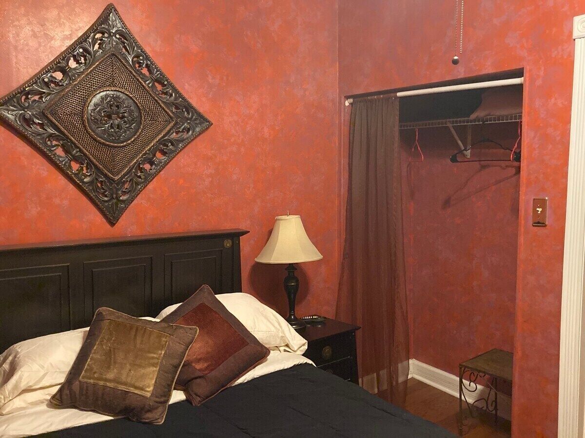 Quarto com cama, mesa de cabeceira, abajur, espelho e guarda-roupa.