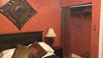 Quarto com cama, mesa de cabeceira, abajur, espelho e guarda-roupa.