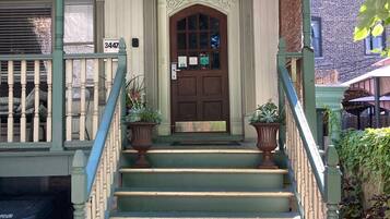 Un edificio de dos pisos con fachada verde, una puerta marrón y una escalera con barandilla.