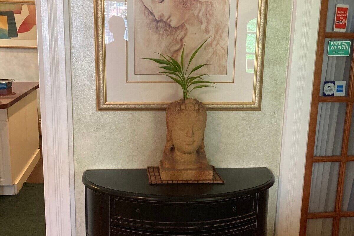 A framed artwork of a woman's face above a dark wooden console table with a potted plant.