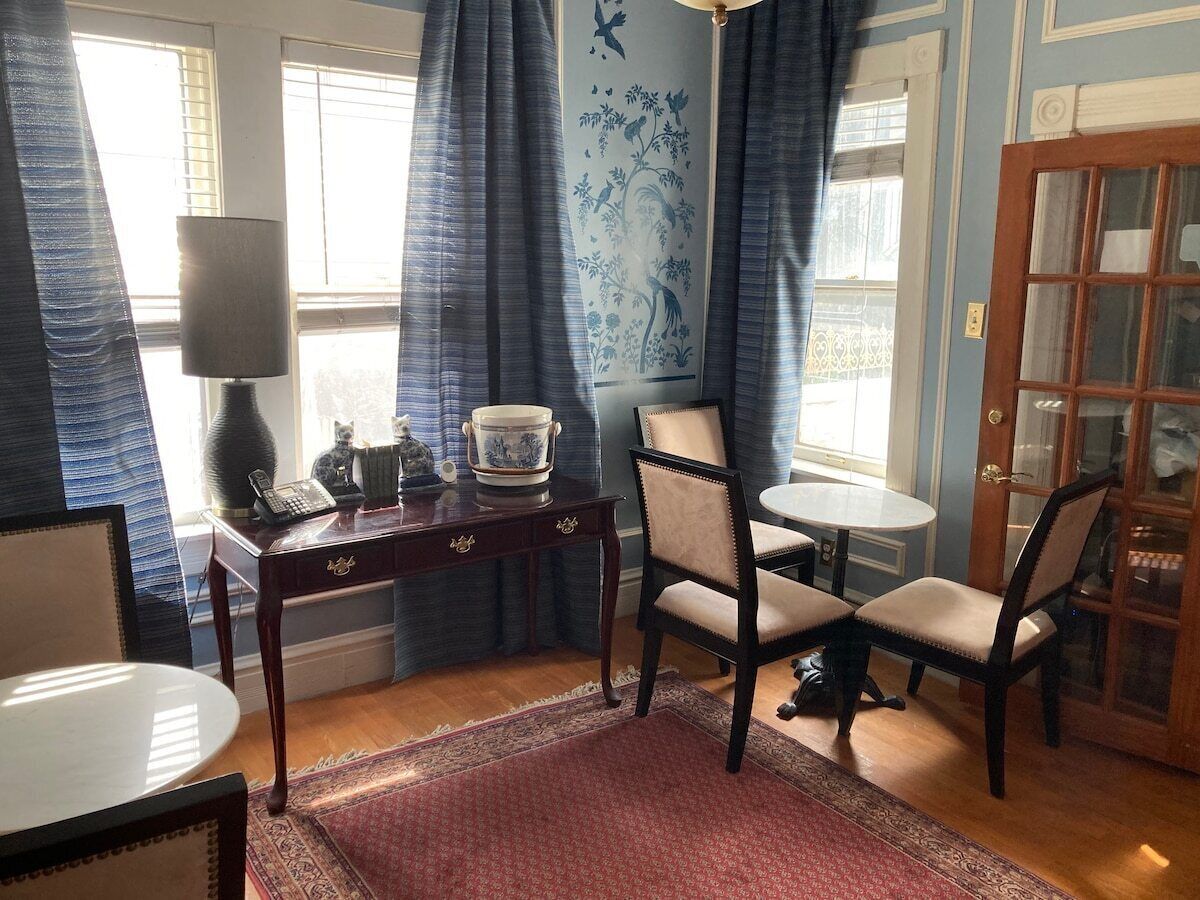 Una habitación con una mesa de comedor, dos sillas, una mesita con adornos, una lámpara y un tapete estampado.