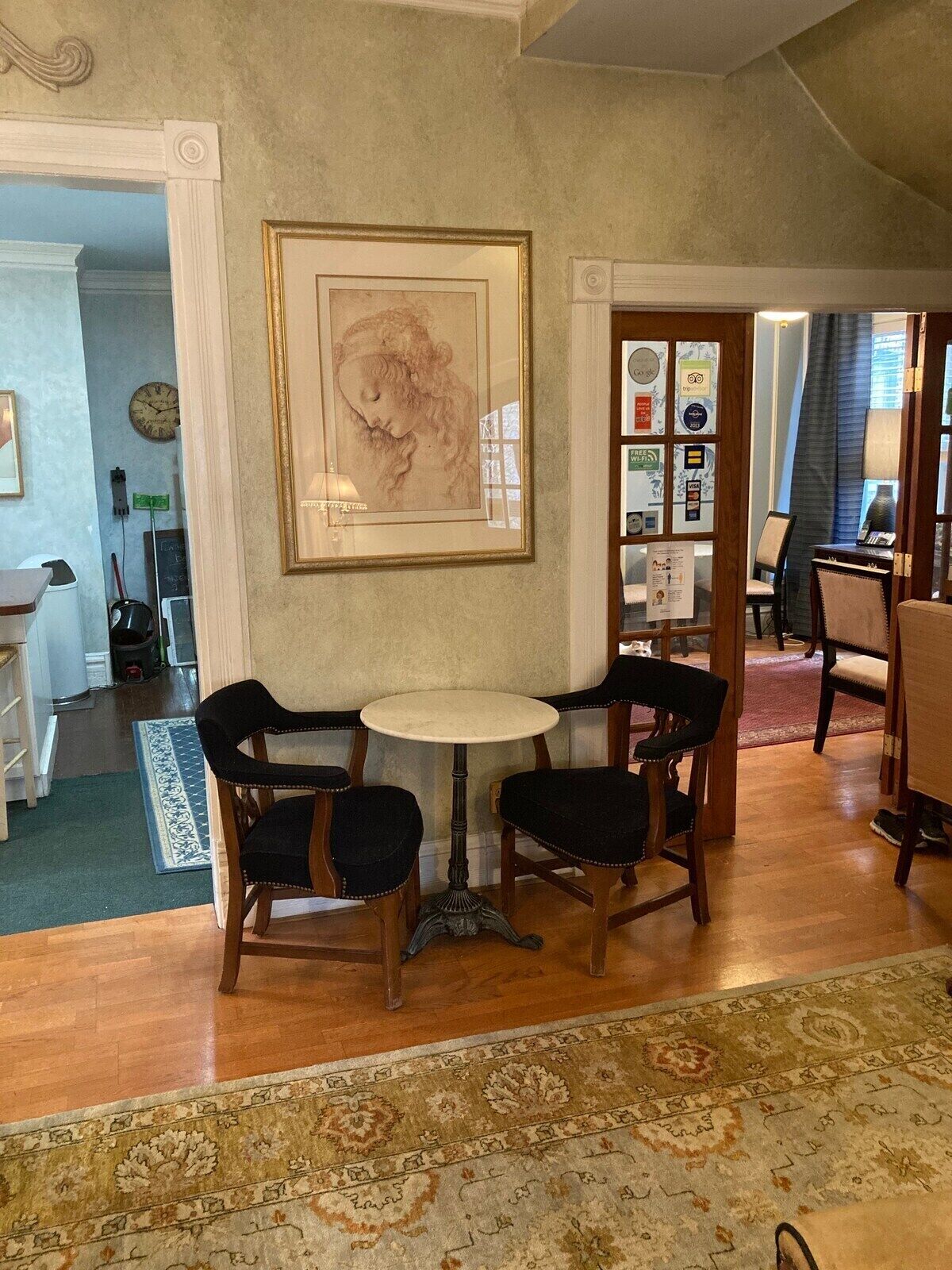 Un comedor con una mesa redonda y cuatro sillas, una obra de arte grande enmarcadas en la pared, y un tapete estampado en el suelo.