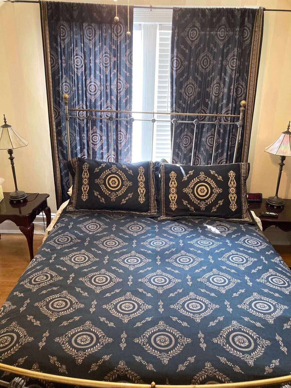 Una cama con colcha azul y dorada estampada, cojines a juego y cabecera de metal.