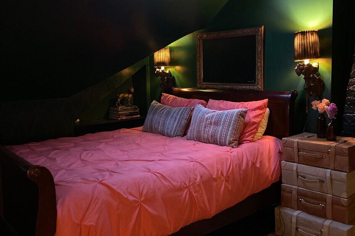A bedroom with a skylight, a bed with pink bedding, a patterned rug, and a stack of suitcases.