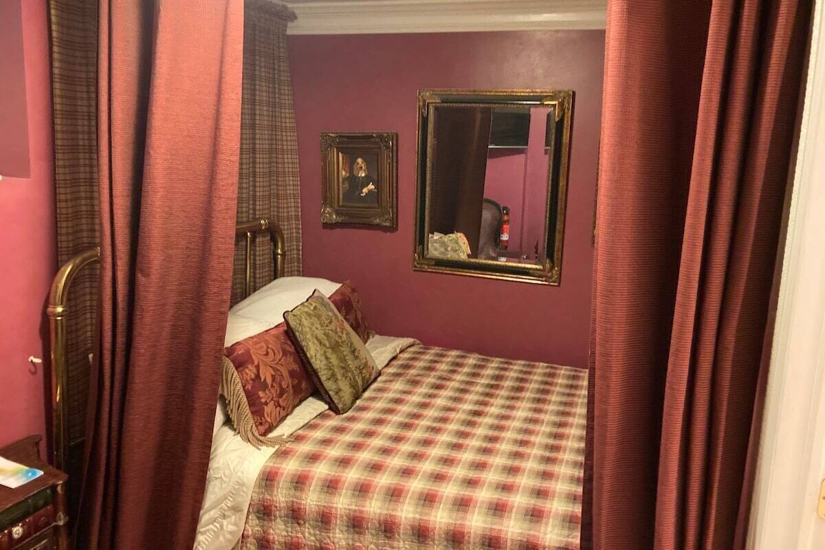 A bedroom with a bed, curtains, a mirror, and a picture frame on the wall.