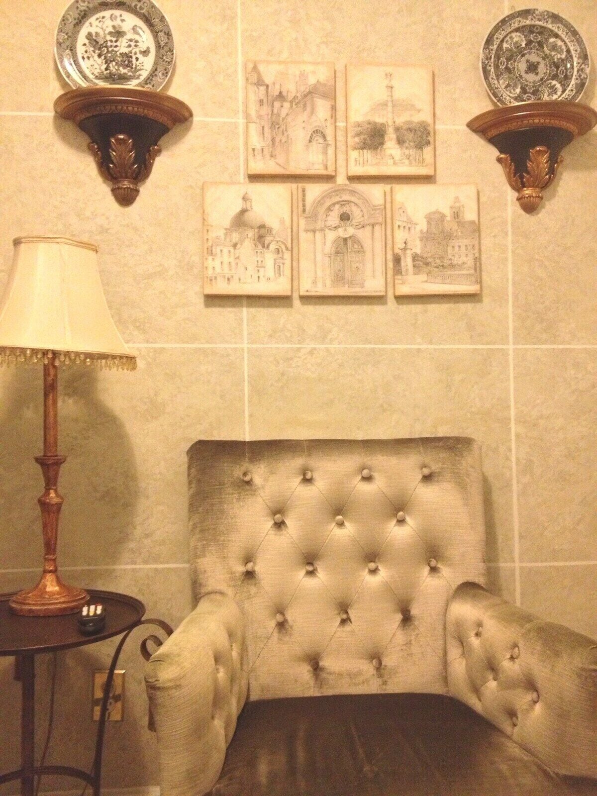 A room with a tufted armchair, a lamp, and wall-mounted plates with artwork.