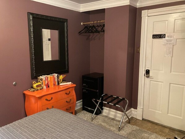 A bedroom with a bed, an orange dresser, a black desk, a mirror, a coat rack, and a white door. - The Villa Toscana (Chicago)